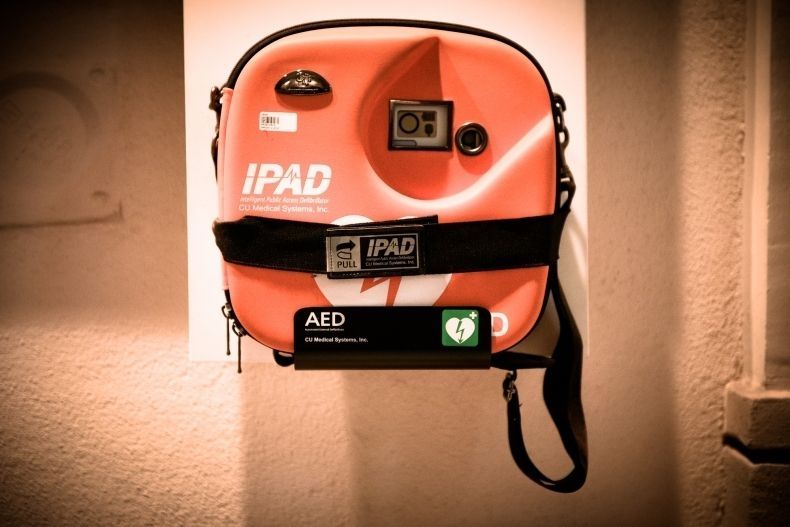 Pomarańczowy defibrylator AED zawieszony na ścianie.